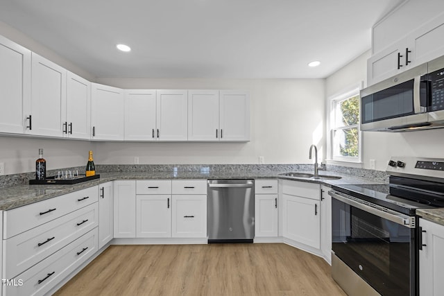 kitchen with light wood-type flooring, stone counters, appliances with stainless steel finishes, white cabinets, and a sink