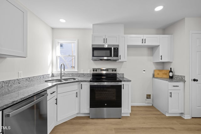 kitchen featuring light stone countertops, light wood-style flooring, a sink, white cabinets, and appliances with stainless steel finishes