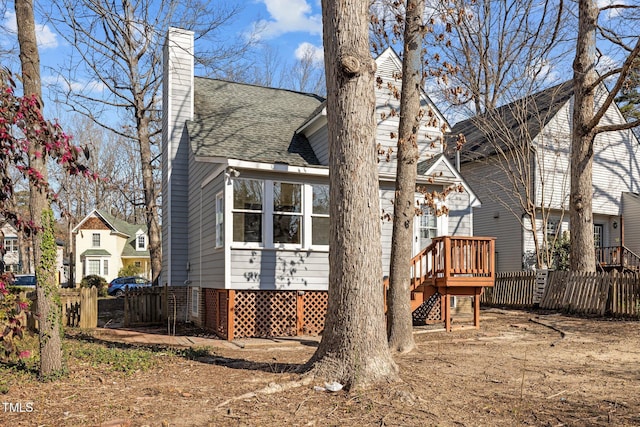 view of home's exterior featuring a wooden deck, fence, a chimney, and a shingled roof