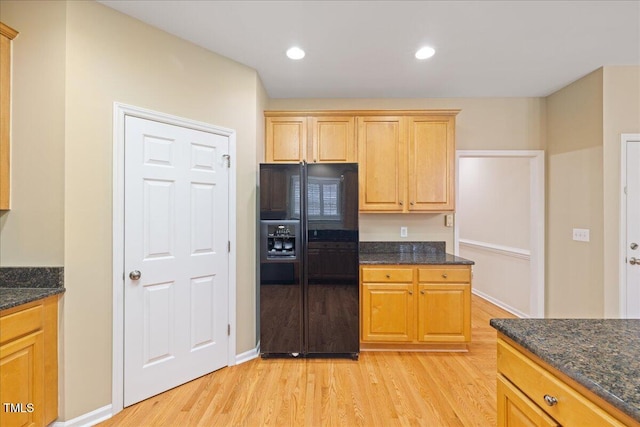 kitchen with recessed lighting, dark stone counters, light wood-style flooring, and black fridge