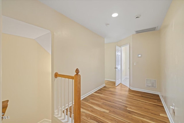 hallway with wood finished floors, an upstairs landing, visible vents, and baseboards