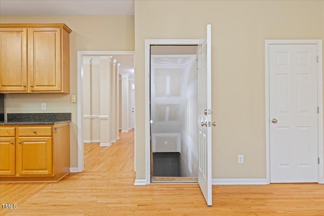 kitchen with dark stone countertops, light wood-type flooring, and baseboards