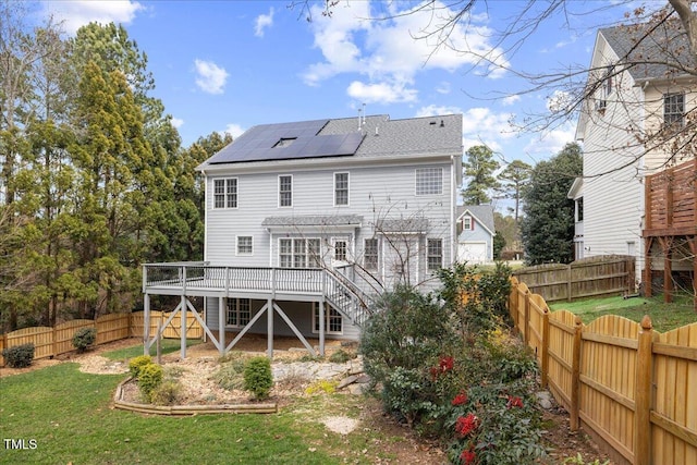 back of house featuring solar panels, stairs, a fenced backyard, a yard, and a deck