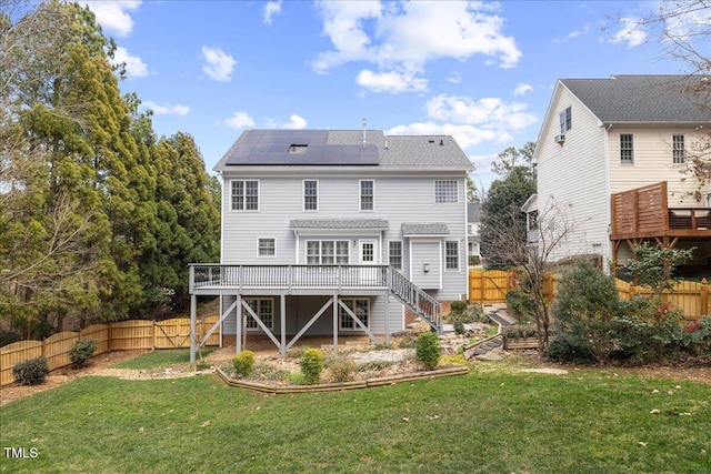 rear view of property featuring roof mounted solar panels, a wooden deck, and a fenced backyard