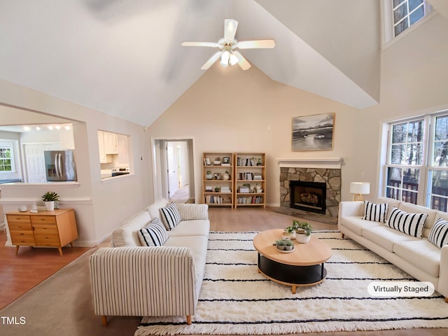 living room with a stone fireplace, a ceiling fan, wood finished floors, and high vaulted ceiling