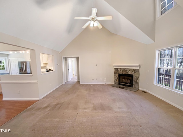 unfurnished living room with high vaulted ceiling, a ceiling fan, a fireplace, baseboards, and light colored carpet