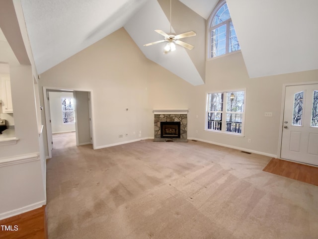 unfurnished living room with a ceiling fan, visible vents, baseboards, a stone fireplace, and light colored carpet