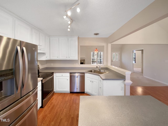 kitchen with a peninsula, a sink, stainless steel appliances, white cabinetry, and light wood-type flooring