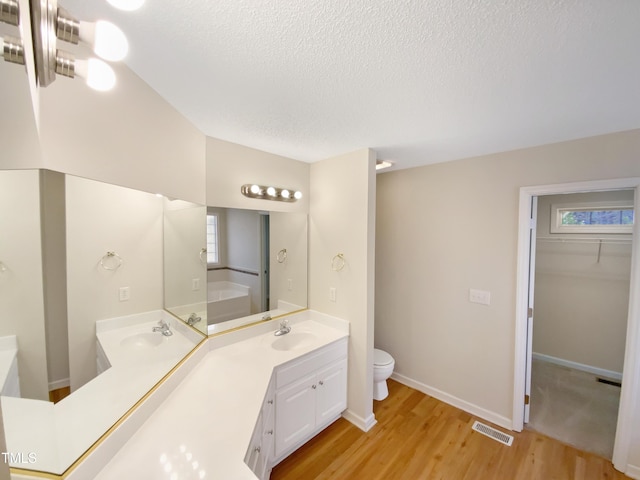 bathroom with visible vents, toilet, a sink, a textured ceiling, and wood finished floors