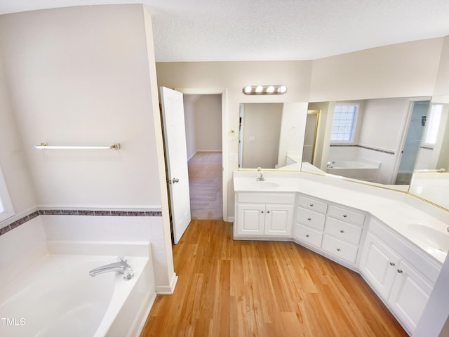 bathroom featuring a sink, a textured ceiling, wood finished floors, double vanity, and a bath