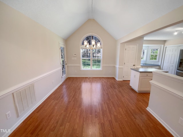 unfurnished dining area featuring lofted ceiling, wood finished floors, visible vents, and a chandelier