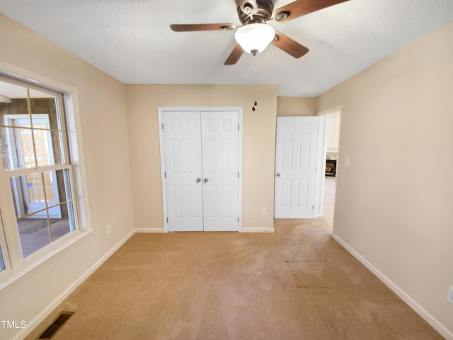 unfurnished bedroom featuring visible vents, light carpet, a textured ceiling, a closet, and baseboards