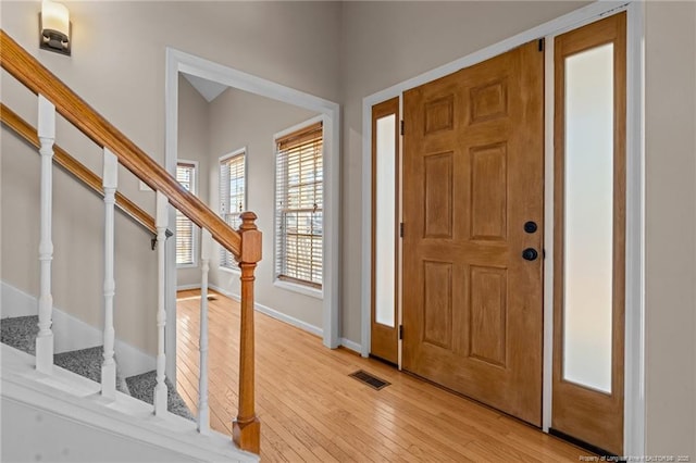 entrance foyer with light wood finished floors, stairway, visible vents, and baseboards