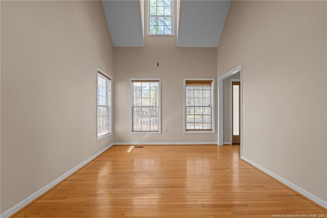 empty room with baseboards, light wood-style floors, and a towering ceiling