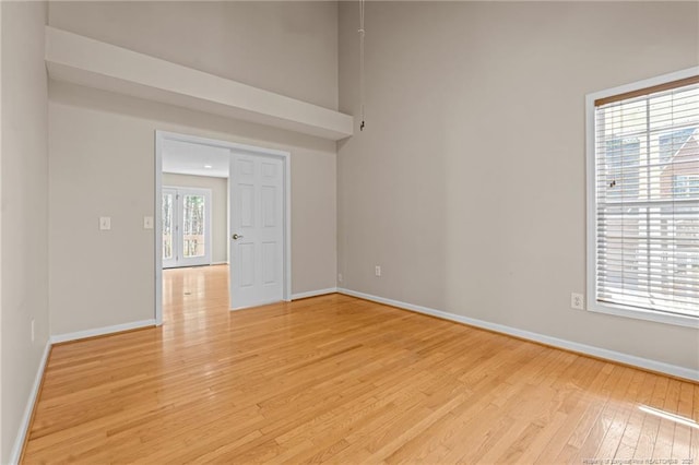 unfurnished room with a high ceiling, baseboards, and light wood finished floors