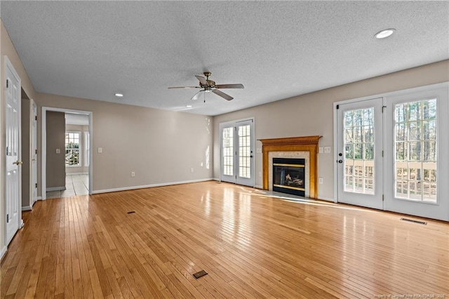 unfurnished living room featuring a fireplace with flush hearth, a ceiling fan, a textured ceiling, hardwood / wood-style floors, and baseboards