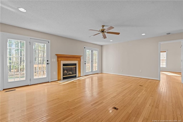 unfurnished living room featuring visible vents, a textured ceiling, a high end fireplace, light wood finished floors, and ceiling fan