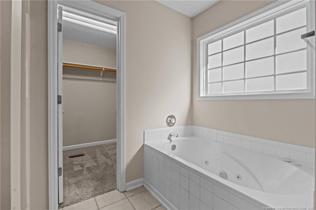 bathroom featuring tile patterned floors, a walk in closet, visible vents, a tub with jets, and baseboards