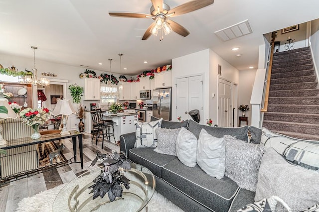 living area featuring recessed lighting, visible vents, ceiling fan with notable chandelier, and stairway