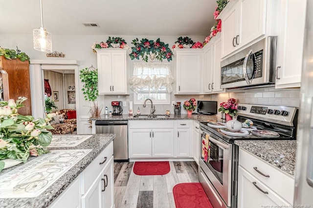 kitchen with light wood-type flooring, a sink, white cabinetry, appliances with stainless steel finishes, and decorative backsplash