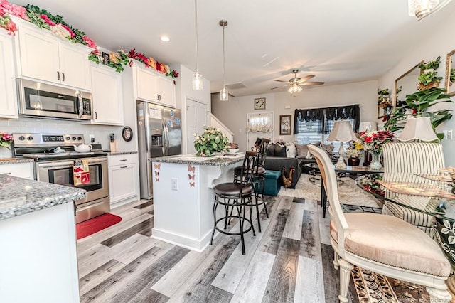 kitchen with stainless steel appliances, white cabinetry, backsplash, and light wood finished floors