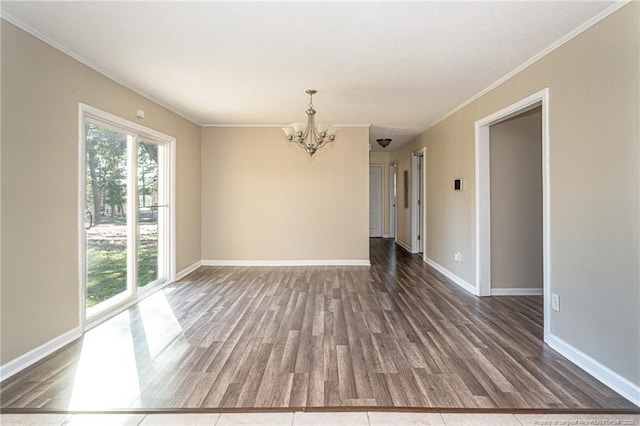 empty room with crown molding, a notable chandelier, wood finished floors, and baseboards