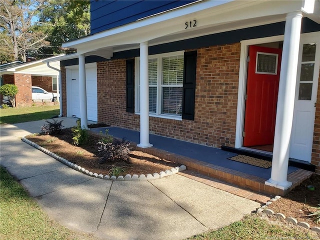 entrance to property featuring a porch, a garage, and brick siding