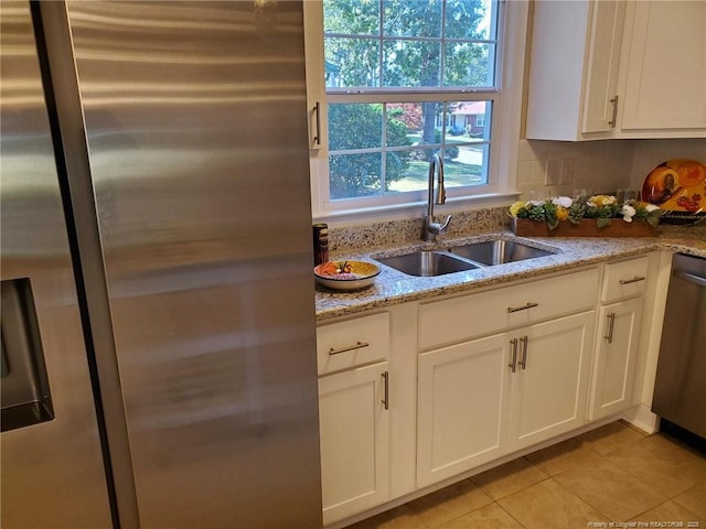 kitchen featuring a sink, stainless steel appliances, white cabinets, light tile patterned floors, and light stone countertops