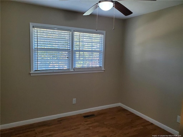 empty room featuring dark wood-style floors, visible vents, ceiling fan, and baseboards