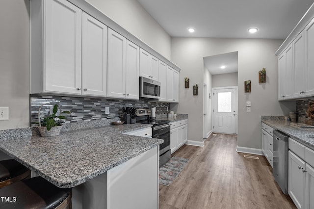 kitchen with tasteful backsplash, light wood-type flooring, a kitchen bar, a peninsula, and stainless steel appliances