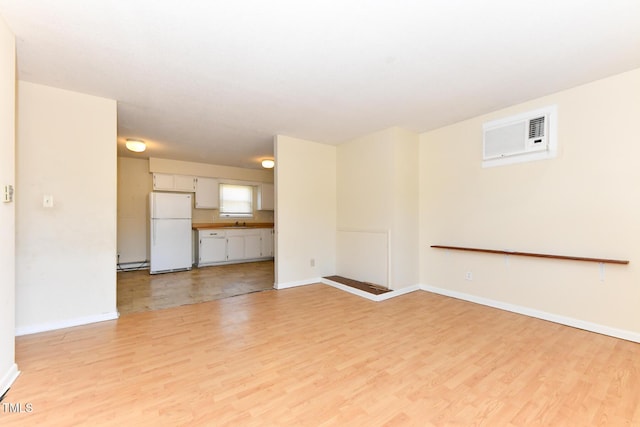 unfurnished living room featuring a wall mounted air conditioner, baseboards, and light wood-style flooring