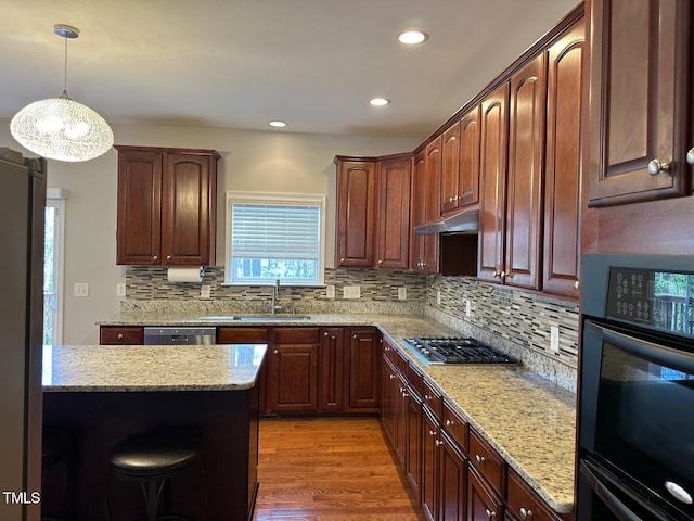 kitchen with light wood finished floors, under cabinet range hood, light stone counters, stainless steel appliances, and a sink