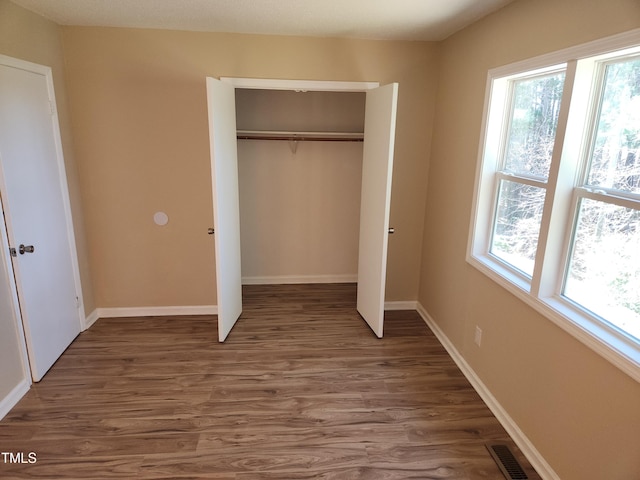 unfurnished bedroom featuring multiple windows, wood finished floors, visible vents, and a closet