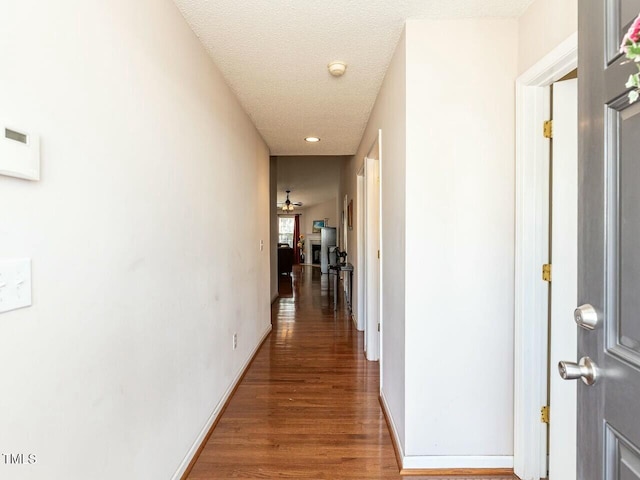 hallway featuring recessed lighting, a textured ceiling, baseboards, and wood finished floors