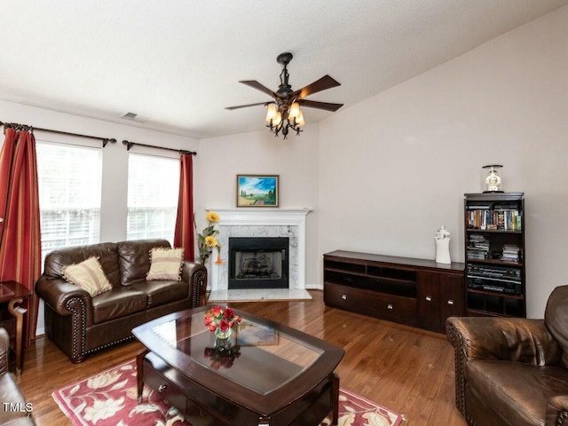 living area featuring a premium fireplace, wood finished floors, visible vents, and ceiling fan