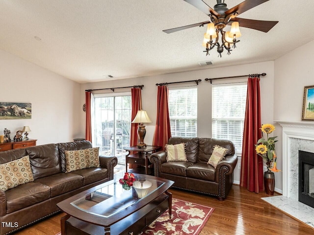 living room featuring visible vents, ceiling fan, a fireplace, wood finished floors, and a textured ceiling