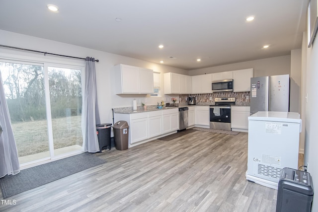 kitchen with white cabinets, light wood-style flooring, tasteful backsplash, and appliances with stainless steel finishes