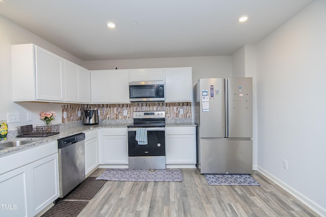 kitchen with tasteful backsplash, white cabinets, stainless steel appliances, and light wood-style flooring