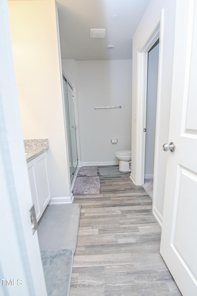 bathroom with baseboards, toilet, a stall shower, wood finished floors, and vanity