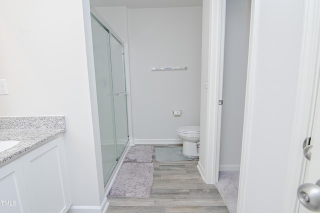 full bathroom featuring toilet, a stall shower, wood finished floors, baseboards, and vanity