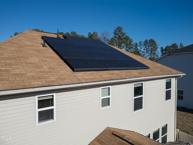 view of side of home with solar panels and roof with shingles