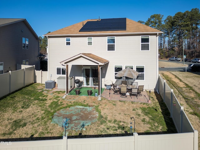 back of house featuring solar panels, central AC unit, a yard, and a fenced backyard