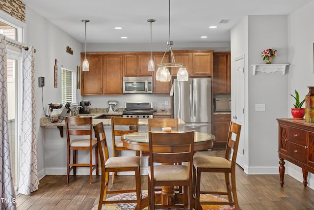 kitchen with hanging light fixtures, stainless steel appliances, dark wood-type flooring, and light stone counters