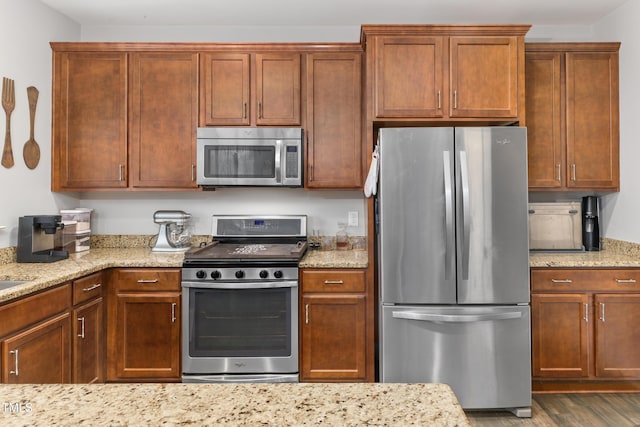 kitchen featuring light stone counters, wood finished floors, brown cabinets, and appliances with stainless steel finishes