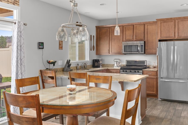 kitchen featuring light stone counters, brown cabinets, wood finished floors, stainless steel appliances, and a sink