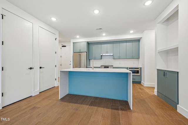 kitchen featuring a center island with sink, stainless steel appliances, light countertops, and light wood-style floors