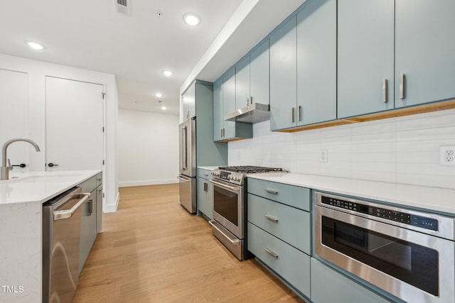 kitchen with light wood-style flooring, a sink, under cabinet range hood, appliances with stainless steel finishes, and tasteful backsplash