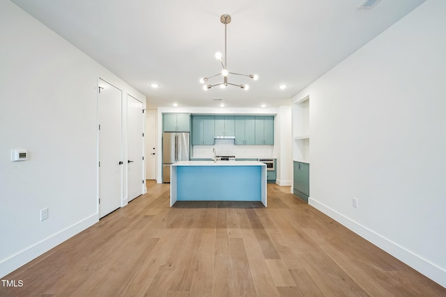 kitchen with baseboards, light wood-style flooring, an island with sink, stainless steel refrigerator, and decorative backsplash