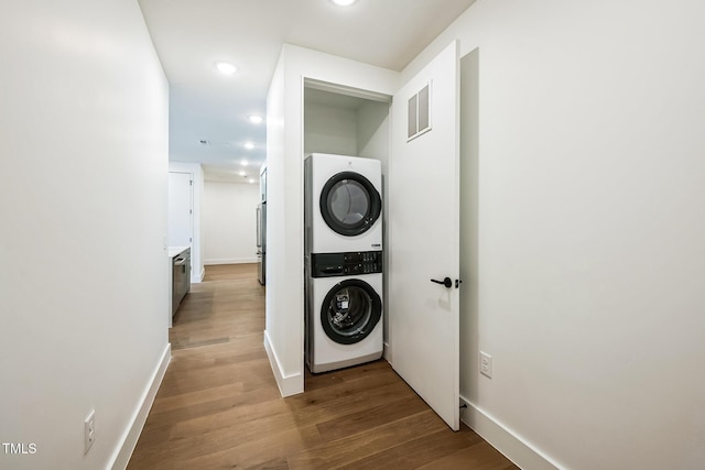 clothes washing area with baseboards, visible vents, stacked washing maching and dryer, and light wood-style floors