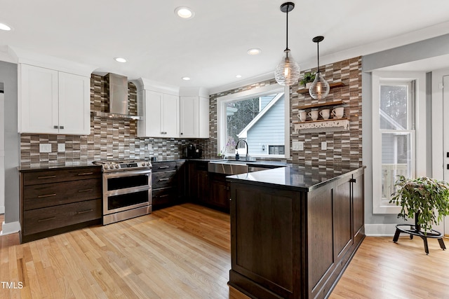 kitchen with double oven range, light wood finished floors, decorative backsplash, dark brown cabinets, and wall chimney exhaust hood